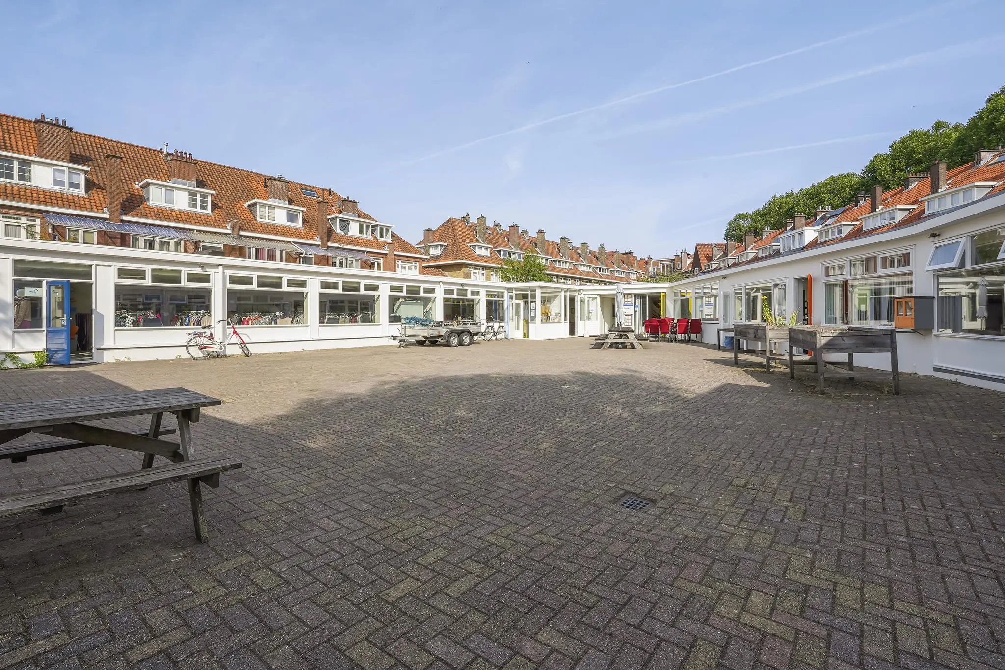 Binnenplein aan de Jacques Perkstraat met bakstenen bestrating, zitbanken en omliggende woningen met rode dakpannen.